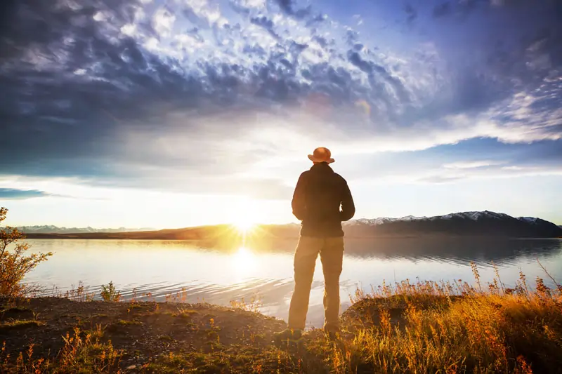 Person steht am See bei Sonnenaufgang und denkt nach, Neuanfang und Heilung nach einer Affäre.