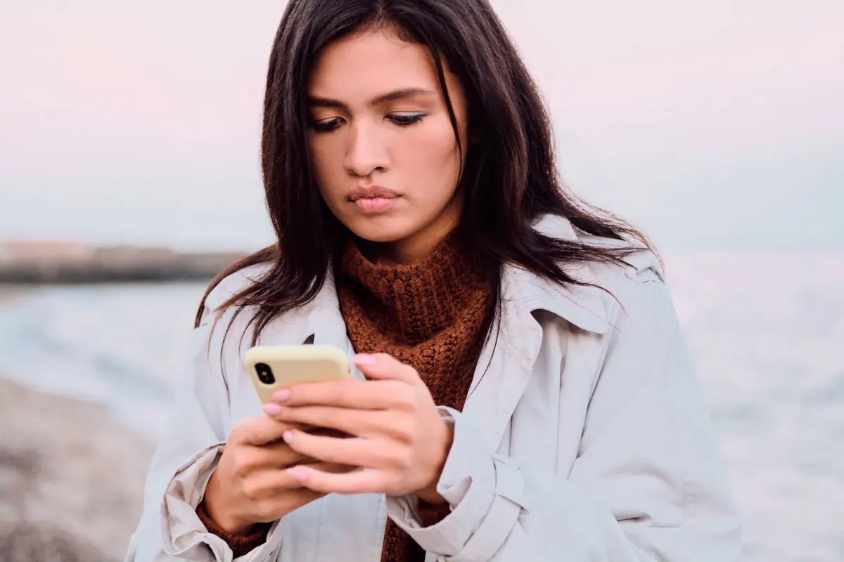 Nachdenkliche Frau schaut auf ihr Handy – Anzeichen, dass der Ex kein Interesse mehr hat.