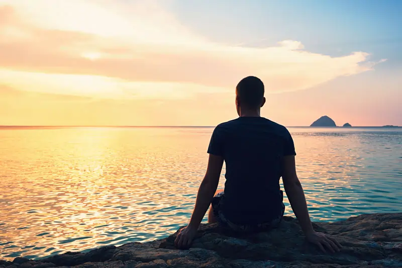 Ein Mann sitzt am Strand und blickt in den Sonnenuntergang, reflektierend darüber, wenn die Liebe weg ist.