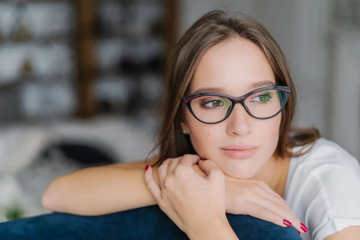 Nachdenkliche Frau mit Brille, die seitlich schaut und den Kopf auf die Hände stützt, symbolisiert Unsicherheit und widersprüchliche Gefühle nach einer Trennung.