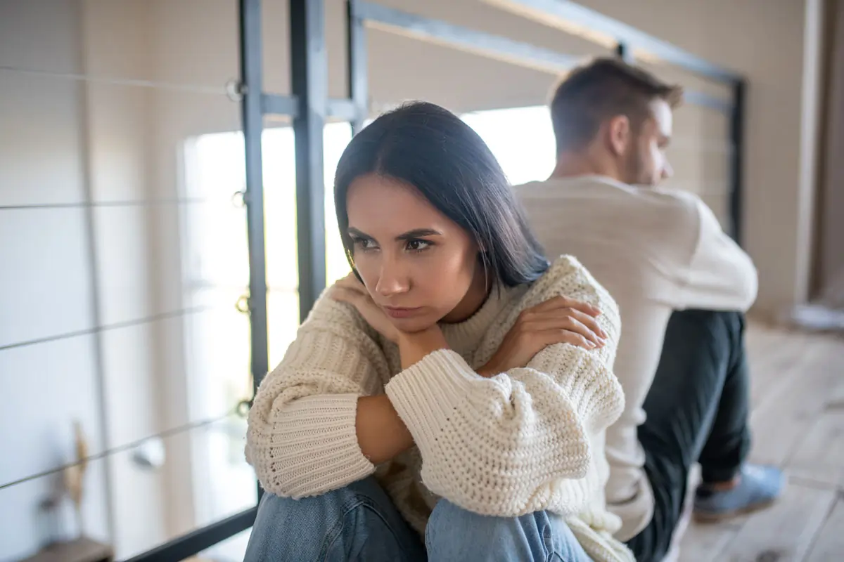 Ein nachdenkliches Paar sitzt mit dem Rücken zueinander, was die emotionale Distanz und Spannungen in einer Beziehung symbolisiert, die durch eine emotionale Affäre entstanden sind.