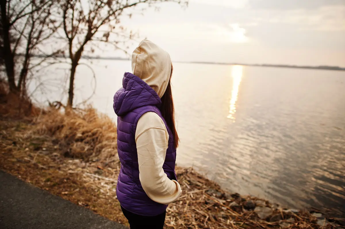 Eine nachdenkliche Person am Seeufer bei Sonnenuntergang, die Ruhe und Selbstreflexion symbolisiert, passend zum Thema emotionale Abhängigkeit.